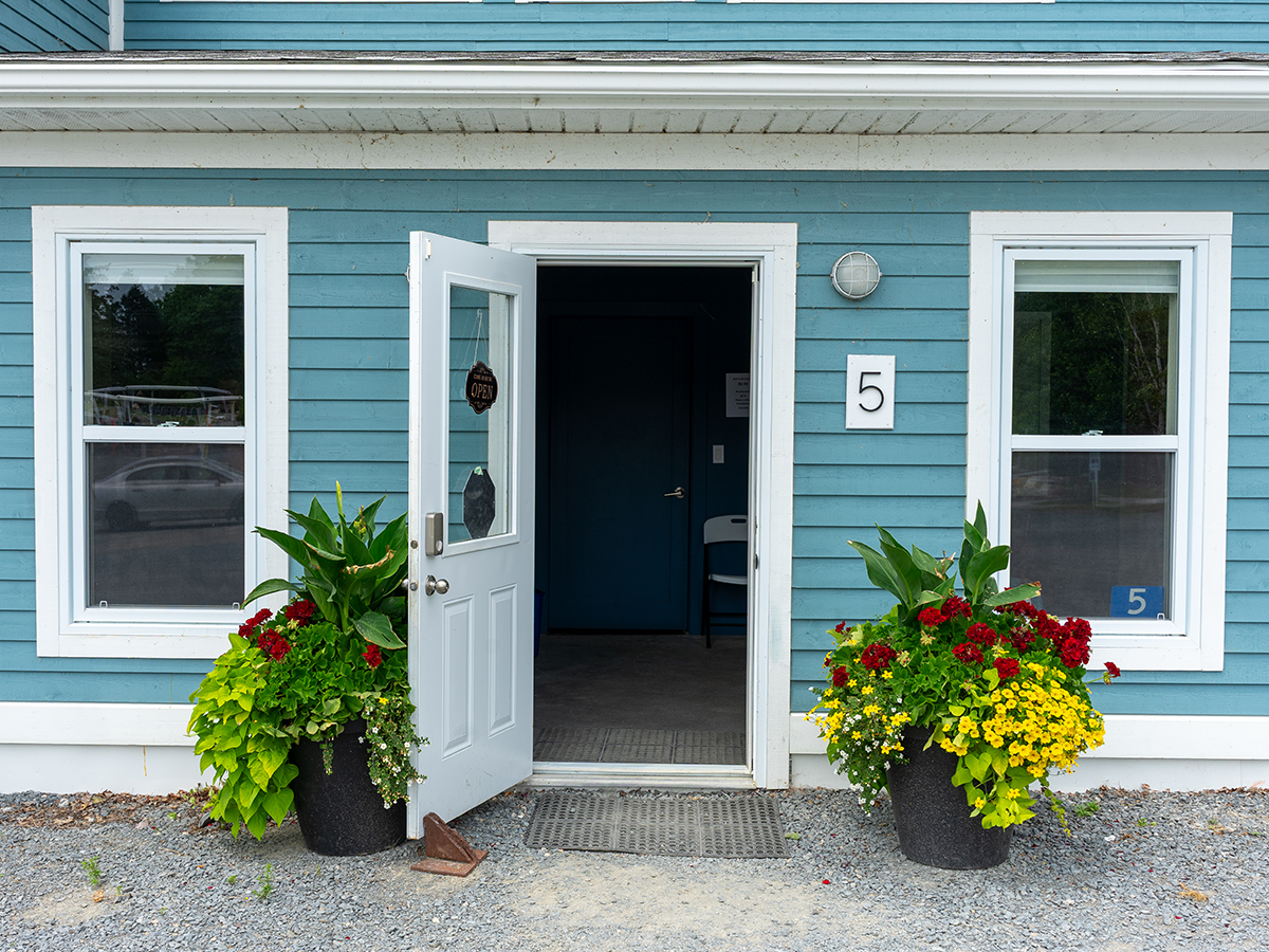 The welcoming front entrance of the Oak Island Interpretive Centre — open door, flower planters, and the house number 5 at 5 Oak Island Drive