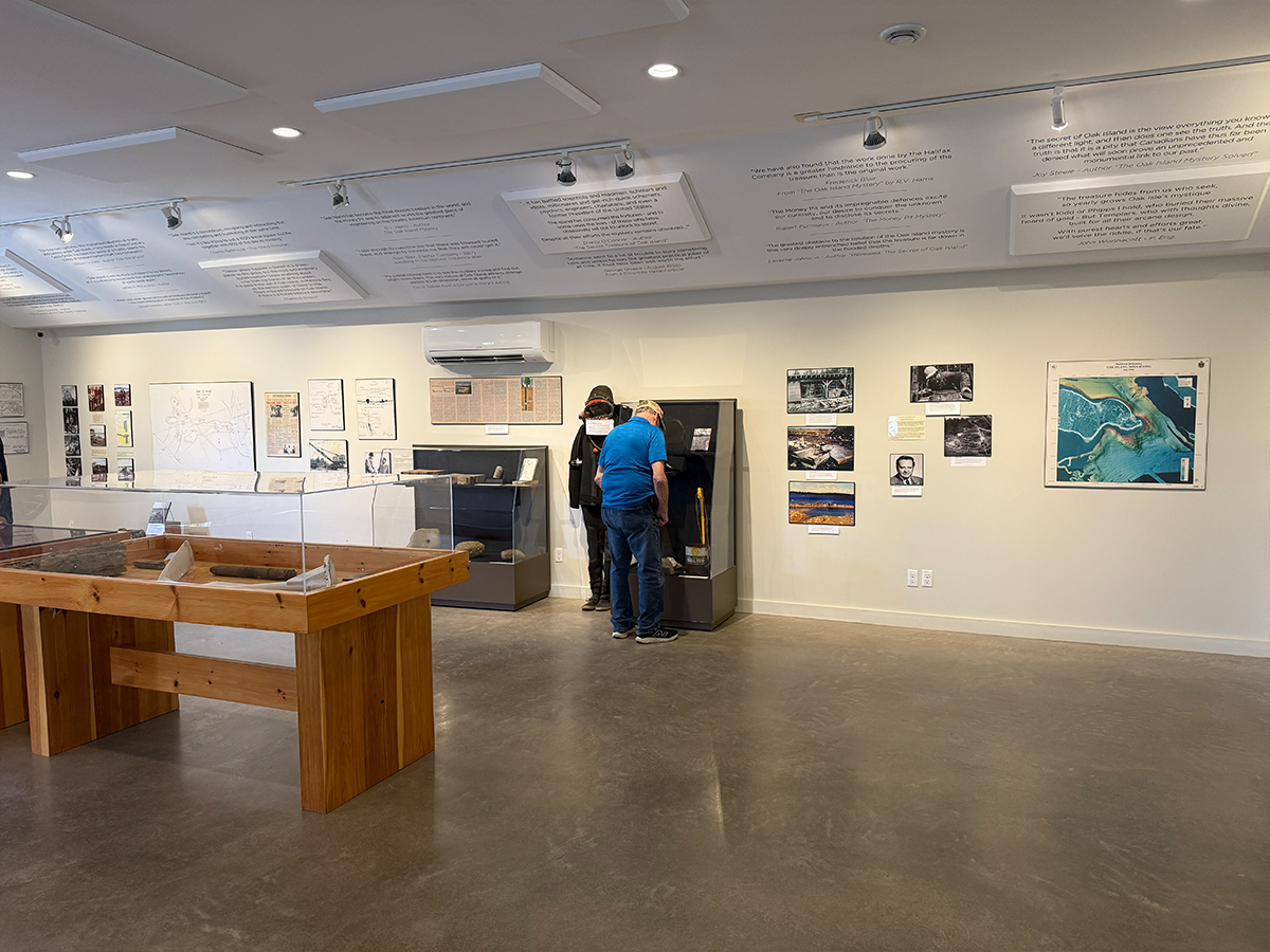 Guests gathered around an interactive Money Pit display cabinet, with an aerial view of Oak Island on the wall