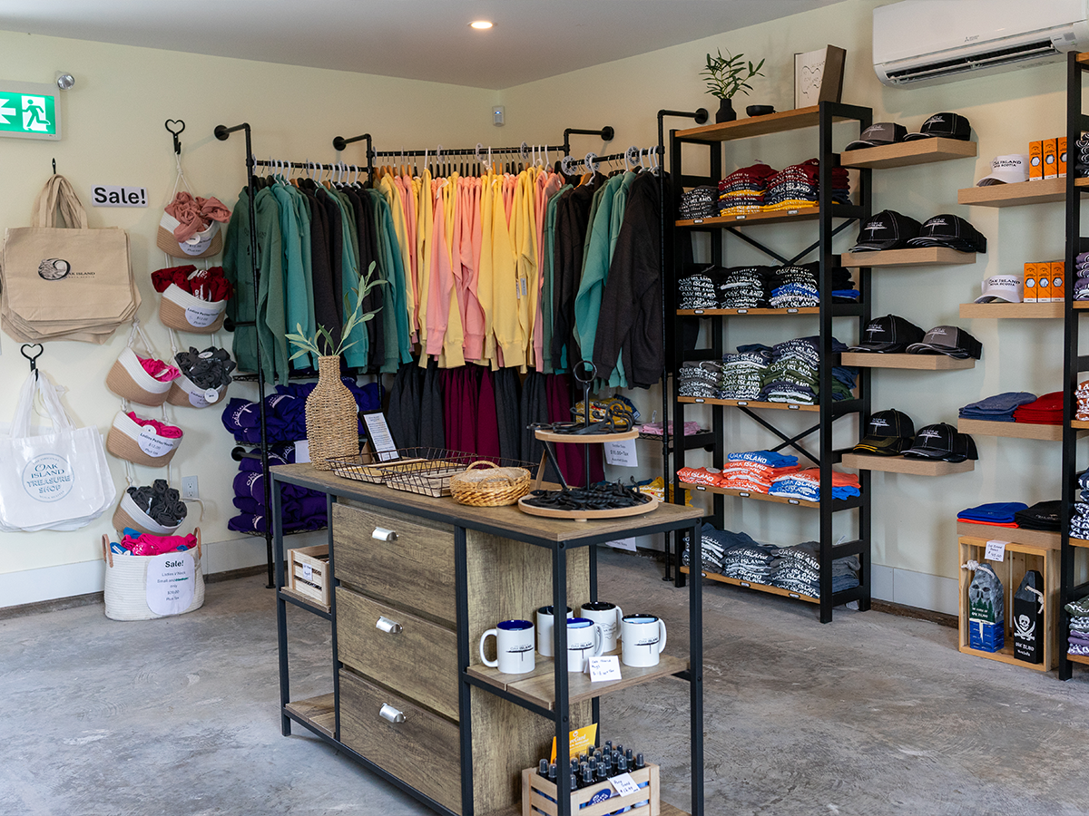 Inside the Oak Island Treasure Shop — racks of colourful Oak Island hoodies and shelves of t-shirts, hats, and mugs
